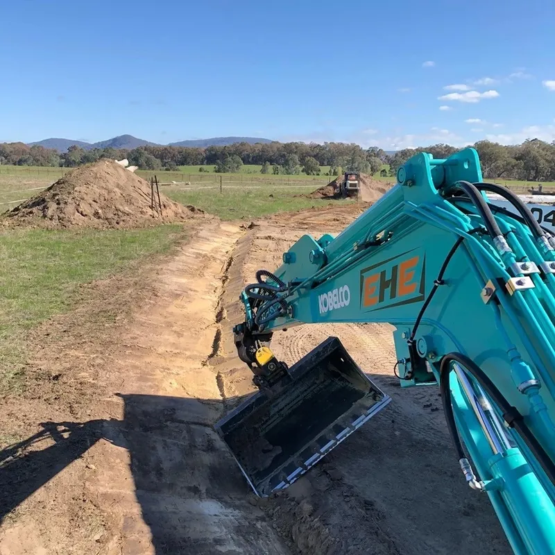 Earth Haul Excavations branded Kobelco excavator on a rural Benalla earthworks site with mountains in the background