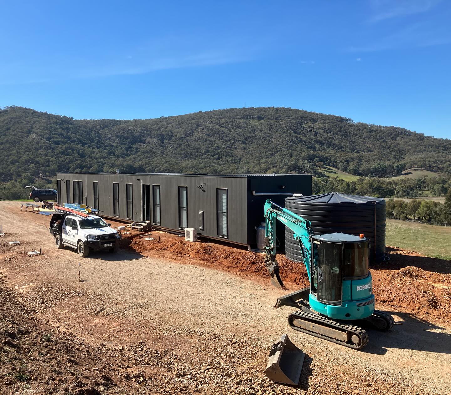 Branded Earth Haul Excavations Kobelco and ute on a rural cabin build with mountain backdrop
