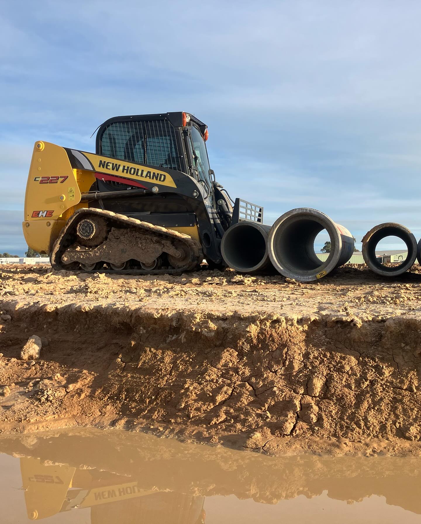 New Holland skid steer track loader on site with large concrete drainage pipes